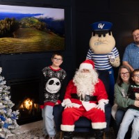 Boy sitting on mom's lap with brother next to Santa and dad behind chair